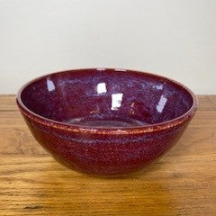 Red ceramic bowl on a wooden surface with a white background